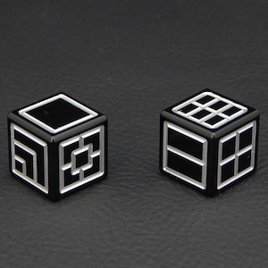 May include: Two black dice with white geometric designs. The dice are on a black surface.