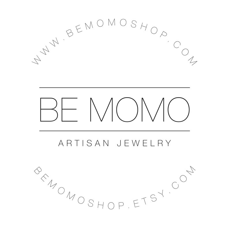 Puede incluir: Logotipo minimalista en blanco y negro. El texto "BE MOMO" se encuentra sobre "ARTISAN JEWELRY". Textos curvos arriba y abajo dicen "www.bemomoshop.com" y "bemomoshop.etsy.com". Dise&ntilde;o limpio y moderno.