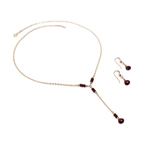 Puede incluir: Un conjunto de collar y pendientes de color dorado. El collar presenta una delicada cadena con peque&ntilde;as piedras preciosas rojas redondas y un colgante m&aacute;s largo con una gema en forma de l&aacute;grima. Los pendientes a juego tienen un dise&ntilde;o similar.