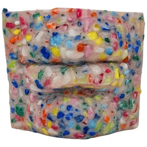 May include: A rectangular block composed of a light-colored material embedded with colorful, irregular pieces. The colors include blue, yellow, pink, orange, and green. The block has a textured surface and a layered appearance.