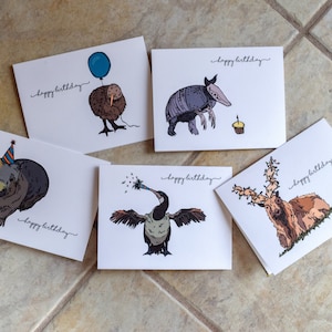 Pu&ograve; includere: Cinque diverse cartoline di compleanno con illustrazioni di animali. Ogni cartolina ha il testo "buon compleanno" scritto su di essa. Gli animali sono un wombat con un cappello da festa, un kiwi con un palloncino, un armadillo, un cormorano che suona un trombetta da festa e un cervo con le corna.