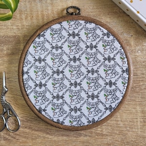 May include: A round wooden embroidery hoop with a white fabric background featuring a repeating pattern of black and white koala bears holding eucalyptus leaves. The koala bears are arranged in a diamond pattern.