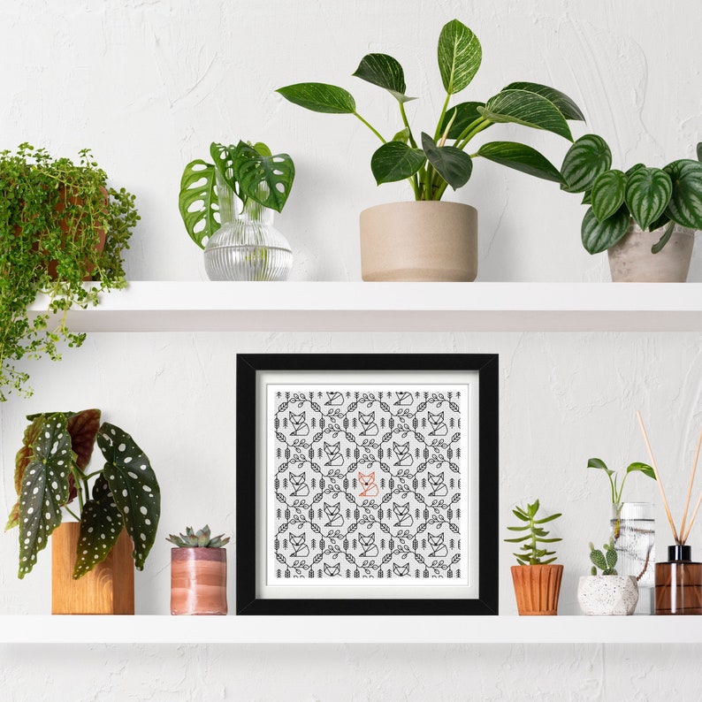 Fox embroidery pattern framed in a square frame on a plant shelf