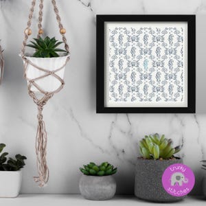 May include: A white ceramic pot with a green succulent plant hangs in a macrame plant hanger. A framed print with a blue and white seahorse pattern is on the wall. Other potted succulents are on a white surface.