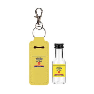 May include: A yellow leatherette keychain holder and a small glass bottle of Louisiana Hot Sauce. The holder has a silver clasp and a key ring. The bottle has a black cap and a yellow label with red, white, and blue accents.