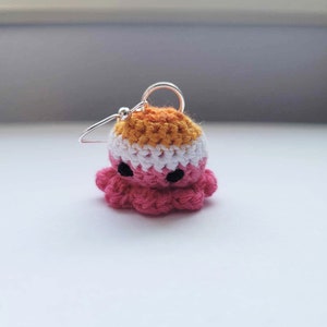 May include: A crocheted octopus earring with a pink body, white stripes, and orange top. The earring is made with a silver hook.