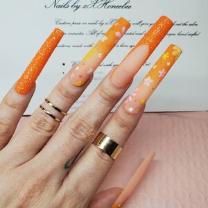 Peut inclure: Longues ongles en gel avec un design floral, de couleur orange et blanche. Les ongles sont ombr&eacute;s avec une pointe paillet&eacute;e. Le texte "Nails by xX Honcebee" est visible en arri&egrave;re-plan.