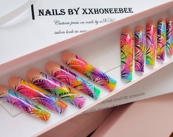 Peut inclure: Un ensemble de dix faux ongles colorés avec un motif en spirale arc-en-ciel et noir. Les ongles sont dans une boîte rose avec le texte "NAILS BY XXHONEEBEE" et "Custom press on nails by XX Ho salon look in min" imprimé sur la boîte.