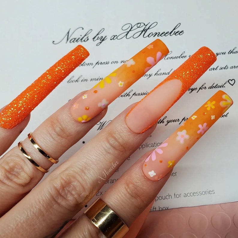 Peut inclure: Des ongles longs avec un art floral orange et rose et des accents de paillettes. Les ongles pr&eacute;sentent un effet d&eacute;grad&eacute;. Le texte "Nails by xX Honcebee" est visible sur l'image.