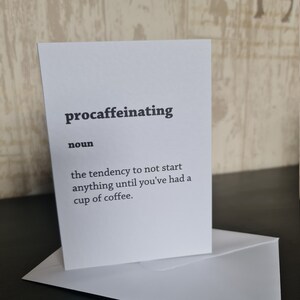 May include: A white card with black text that reads "procaffeinating noun the tendency to not start anything until you've had a cup of coffee."