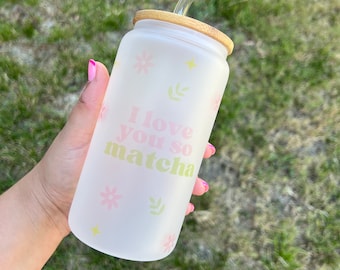 Op de afbeelding: Een gematteerde glazen waterfles met een bamboe deksel en een doorzichtige plastic rietje. De fles heeft een roze en groen bloemenpatroon en de tekst "I love you so matcha".