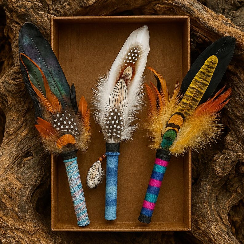 May include: Three decorative feather fans arranged in a brown box. The left fan has dark iridescent feathers with orange accents. The centre fan is white with brown spots and a blue handle. The right fan features yellow, black, and orange feathers.
