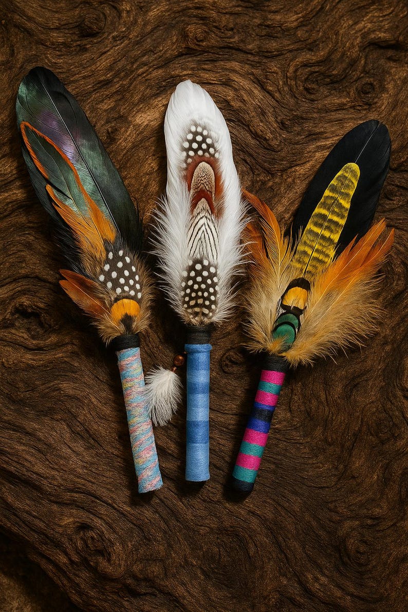 May include: Three decorative feather fans featuring long, layered plumes in shades of white, black, orange, and iridescent green. Each handle is wrapped in colourful thread, with patterns including solid blue, multi-coloured stripes, and pink and teal bands.