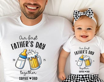 May include: Matching white t-shirts and onesie with the text "Our first Father's Day" and a graphic of a baby bottle and beer mug. The onesie is worn by a baby with a black and white checkered bow and pants. The adult is smiling.