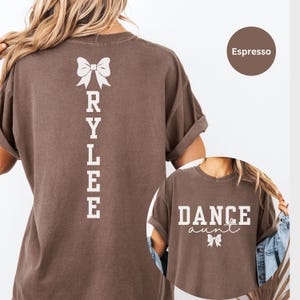 May include: Espresso brown t-shirt with a white bow and the name "RYLEE" spelled vertically down the back. A second espresso brown t-shirt features the text "DANCE aunt" with a white bow.