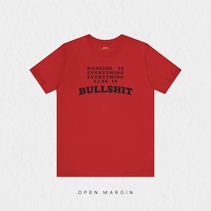 Könnte beinhalten: Ein rotes kurzärmeliges T-Shirt mit schwarzem Text auf der Brust, der DANCING IS EVERYTHING EVERYTHING ELSE IS BULLSHIT lautet. Das Shirt hat einen Rundhalsausschnitt und ein kleines Markenetikett, das innen am Kragen aufgedruckt ist.