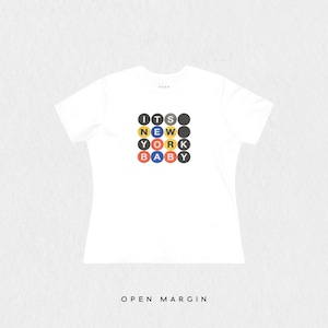 Puede incluir: Una camiseta blanca de manga corta con un dise&ntilde;o gr&aacute;fico de una cuadr&iacute;cula de cuatro por cuatro c&iacute;rculos. Los c&iacute;rculos contienen el texto ITS NEW YORK BABY en letras blancas, con algunos c&iacute;rculos de color amarillo, rojo o azul, y otros gris oscuro.