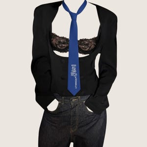 Peut inclure: Une cravate bleue avec le texte blanc KISS ALL THE TIME. DISCO OCCASIONALLY. portée sur un blazer noir court, une brassière en dentelle noire à motifs floraux et un jean bleu foncé. L'ensemble comprend une veste structurée et un jean décontracté.