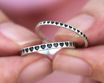May include: Two silver rings with a row of black heart designs around the band.