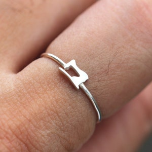 May include: A silver ring featuring a sewing machine silhouette design.