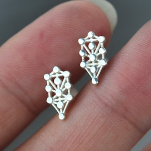 May include: A pair of silver earrings with a geometric tree of life design.