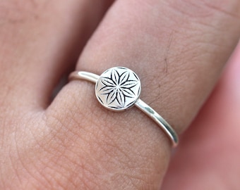 Op de afbeelding: Een zilveren ring met een rond ontwerp met een bloemvormig patroon.