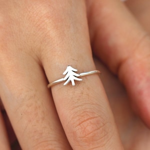 May include: A silver ring with a simple tree design. The ring is on a person's finger.