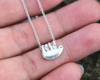 May include: A silver necklace with a small, silver sloth pendant. The sloth is hanging upside down.