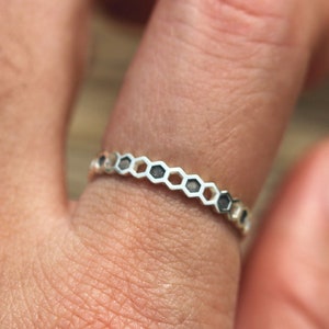 May include: A silver ring with a honeycomb design. The ring is worn on a finger.