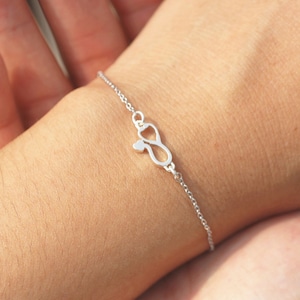 May include: A silver bracelet with an infinity symbol charm. The infinity symbol is made of two hearts intertwined.