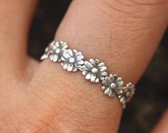 Könnte beinhalten: Ein silberner Ring mit einem zarten Gänseblümchen-Design. Der Ring wird an einem Finger getragen.