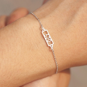 May include: A silver chain bracelet with a rectangular charm that says "520" in a cut-out font.