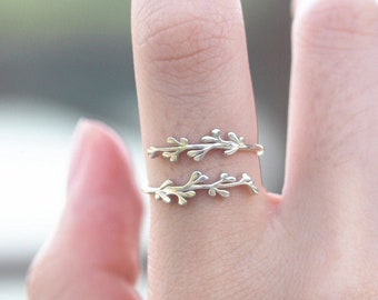 May include: Two delicate silver rings with a leafy design. The rings are worn on the index finger of a hand.