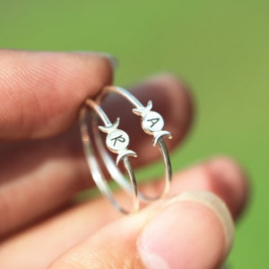 Könnte beinhalten: Zwei silberne Ringe mit Halbmond-Designs und den eingravierten Buchstaben "R" und "A".