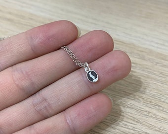 May include: A silver chain necklace with a small oval pendant featuring a black and white silhouette of a bird.