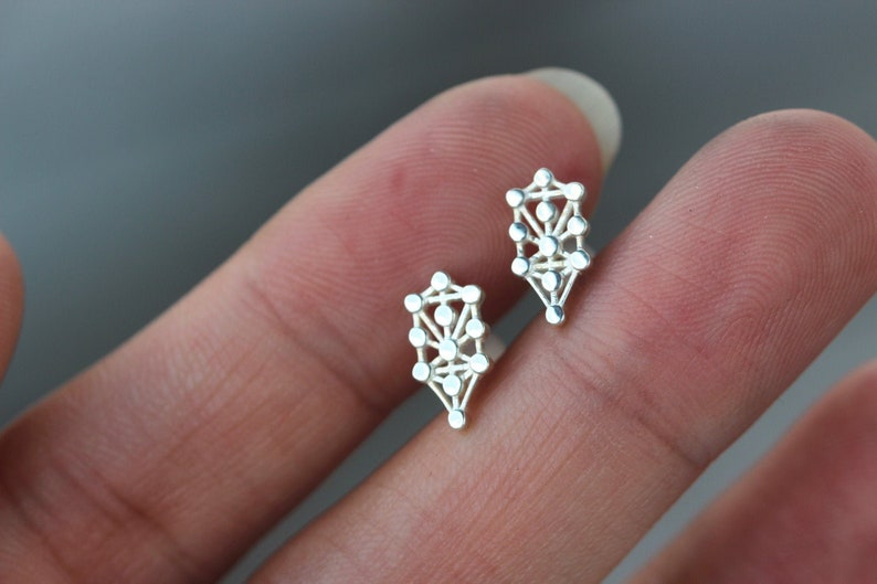 May include: A pair of silver earrings with a geometric tree of life design.