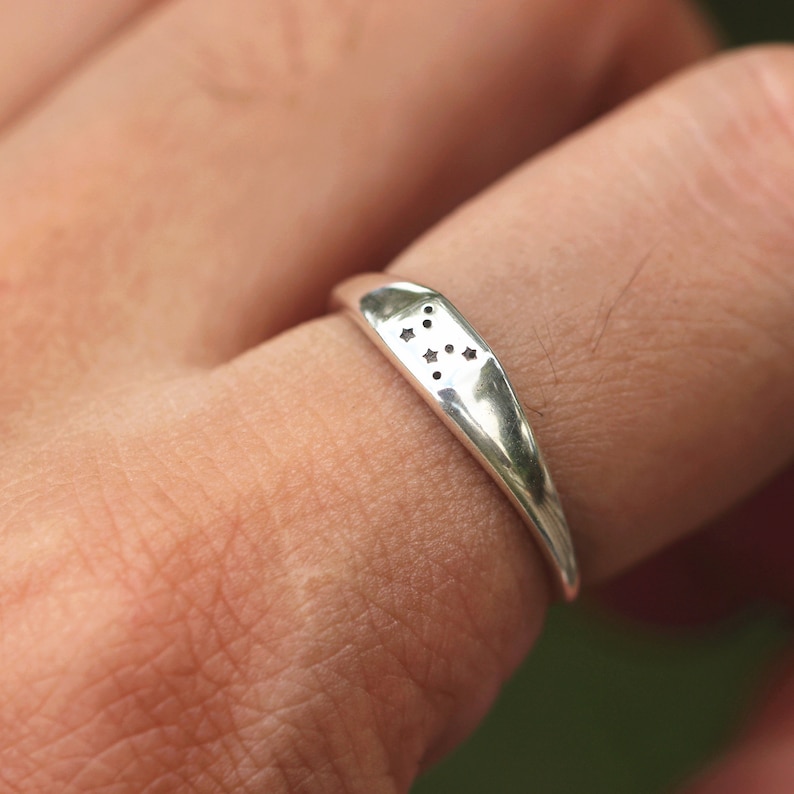 Puede incluir: Un anillo de plata con un dise&ntilde;o de constelaci&oacute;n. El anillo se lleva en un dedo.