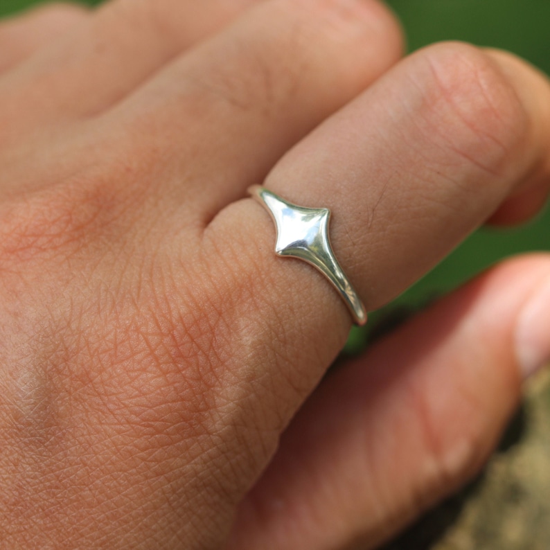 Pode incluir: Um anel de prata com um design pontiagudo em forma de diamante. O anel &eacute; usado em um dedo.