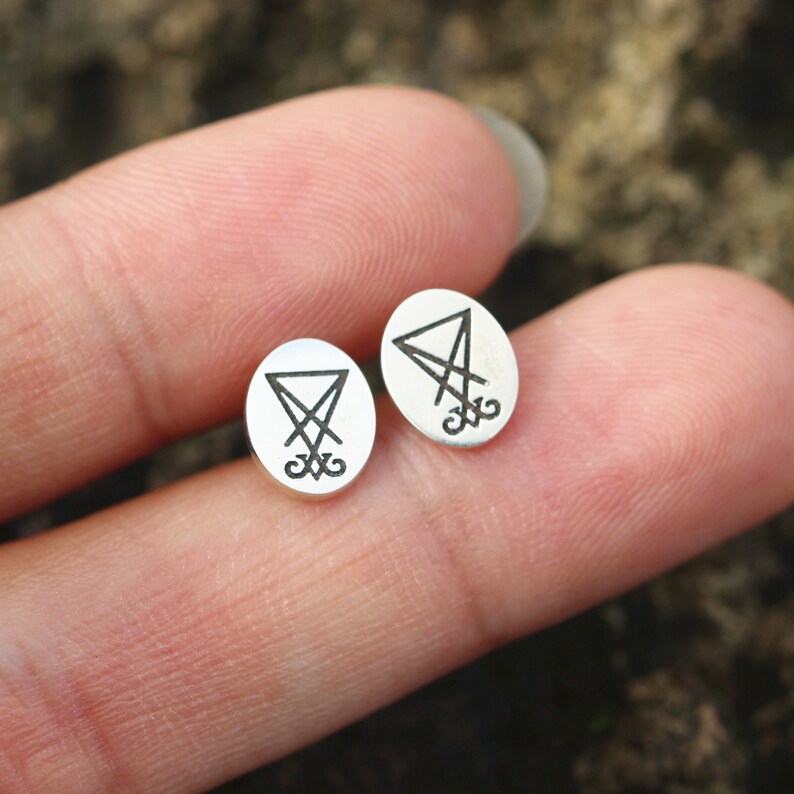 K&ouml;nnte beinhalten: Ein Paar silberne Ohrringe mit einem schwarzen, gravierten Symbol eines Pentagramms mit einem umgekehrten Kreuz darin.
