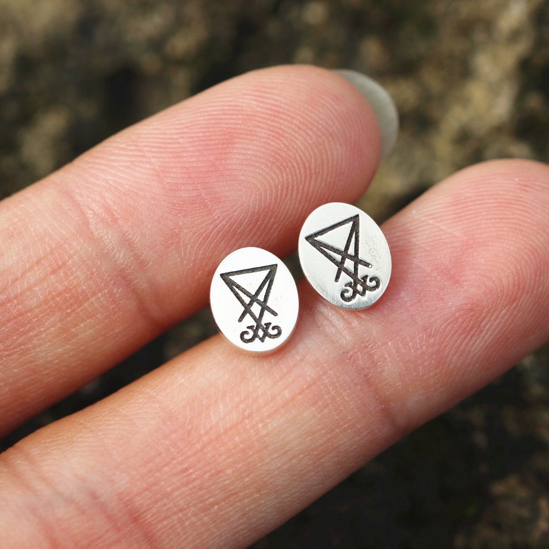 K&ouml;nnte beinhalten: Ein Paar silberne Ohrringe mit einem schwarzen Sigel-Design. Das Sigel ist ein Dreieck mit einem Kreuz darin.