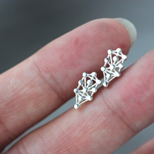 May include: A pair of silver earrings with a geometric design. The earrings are shaped like a teardrop and are made up of small, interconnected circles.