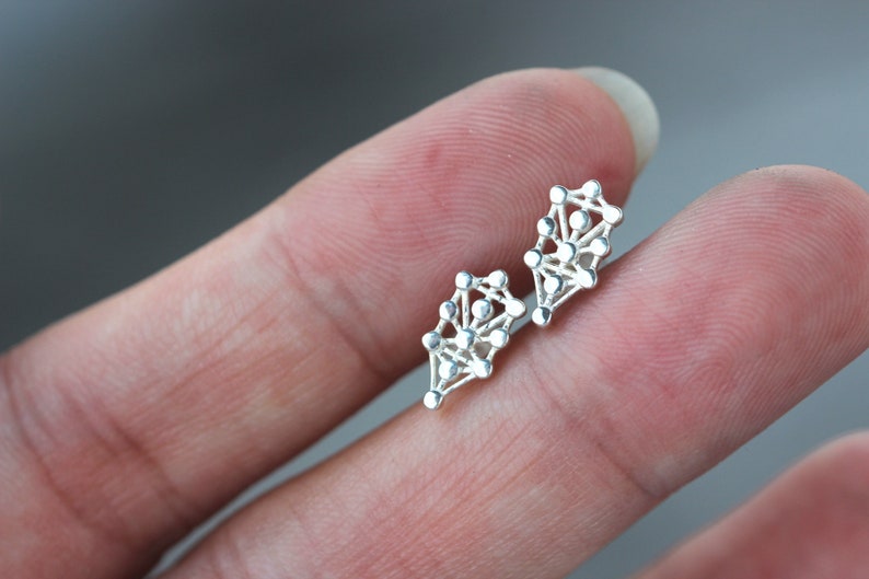 May include: A pair of silver earrings with a geometric design. The earrings are shaped like a teardrop and are made up of small, interconnected circles.