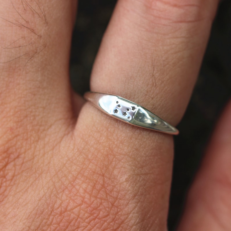 Puede incluir: Un anillo de plata con un dise&ntilde;o de cinco estrellas en la parte superior. El anillo se lleva en un dedo.