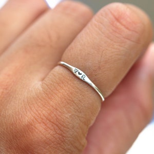 May include: A silver ring with the inscription "TP &hearts; SL" on a person's finger.