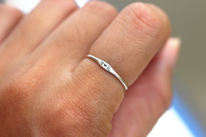 May include: A silver ring with the inscription "TP &hearts; SL" on a person's finger.