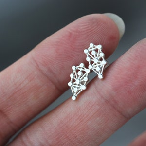 May include: A pair of silver earrings with a geometric design. The earrings are made of small, interconnected circles.