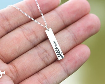 Puede incluir: Un collar plateado con un colgante rectangular con un diseño de árbol negro. El colgante cuelga de una delicada cadena plateada. El collar se muestra sobre un fondo borroso.