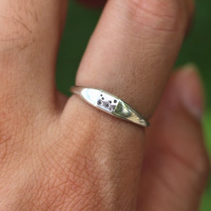 Puede incluir: Un anillo de plata con un peque&ntilde;o dise&ntilde;o rectangular que presenta un grupo de peque&ntilde;os recortes redondos. El anillo se lleva en un dedo.