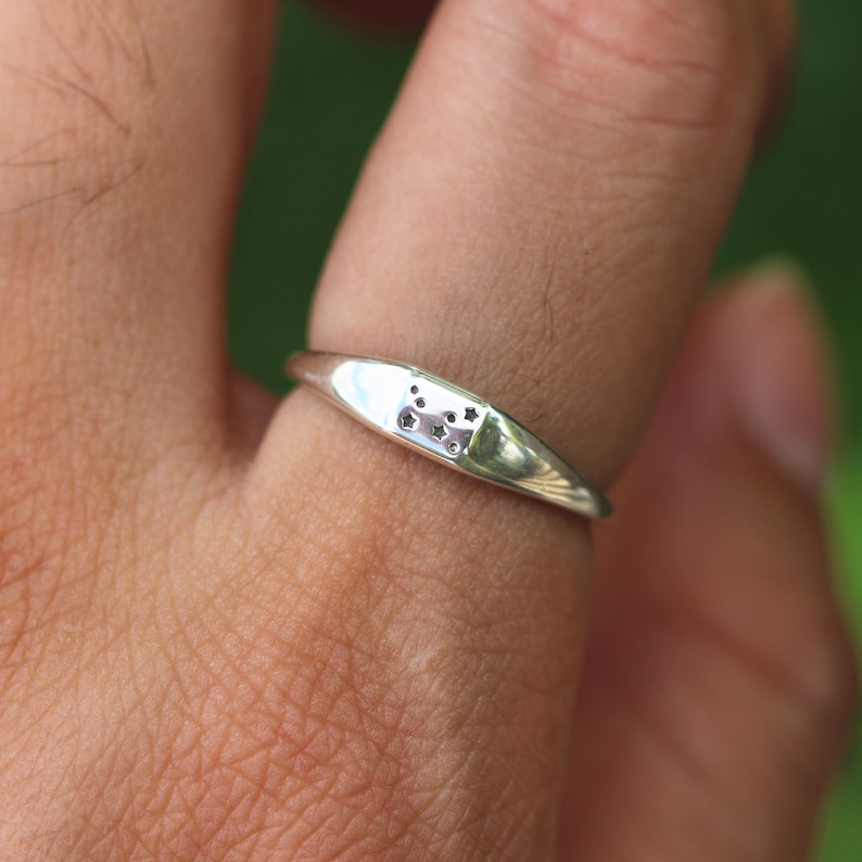 Puede incluir: Un anillo de plata con un peque&ntilde;o dise&ntilde;o rectangular que presenta un grupo de peque&ntilde;os recortes redondos. El anillo se lleva en un dedo.