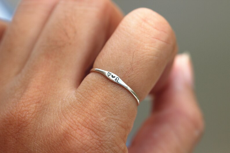 May include: A silver ring with the zodiac signs Virgo and Leo and a heart symbol between them.